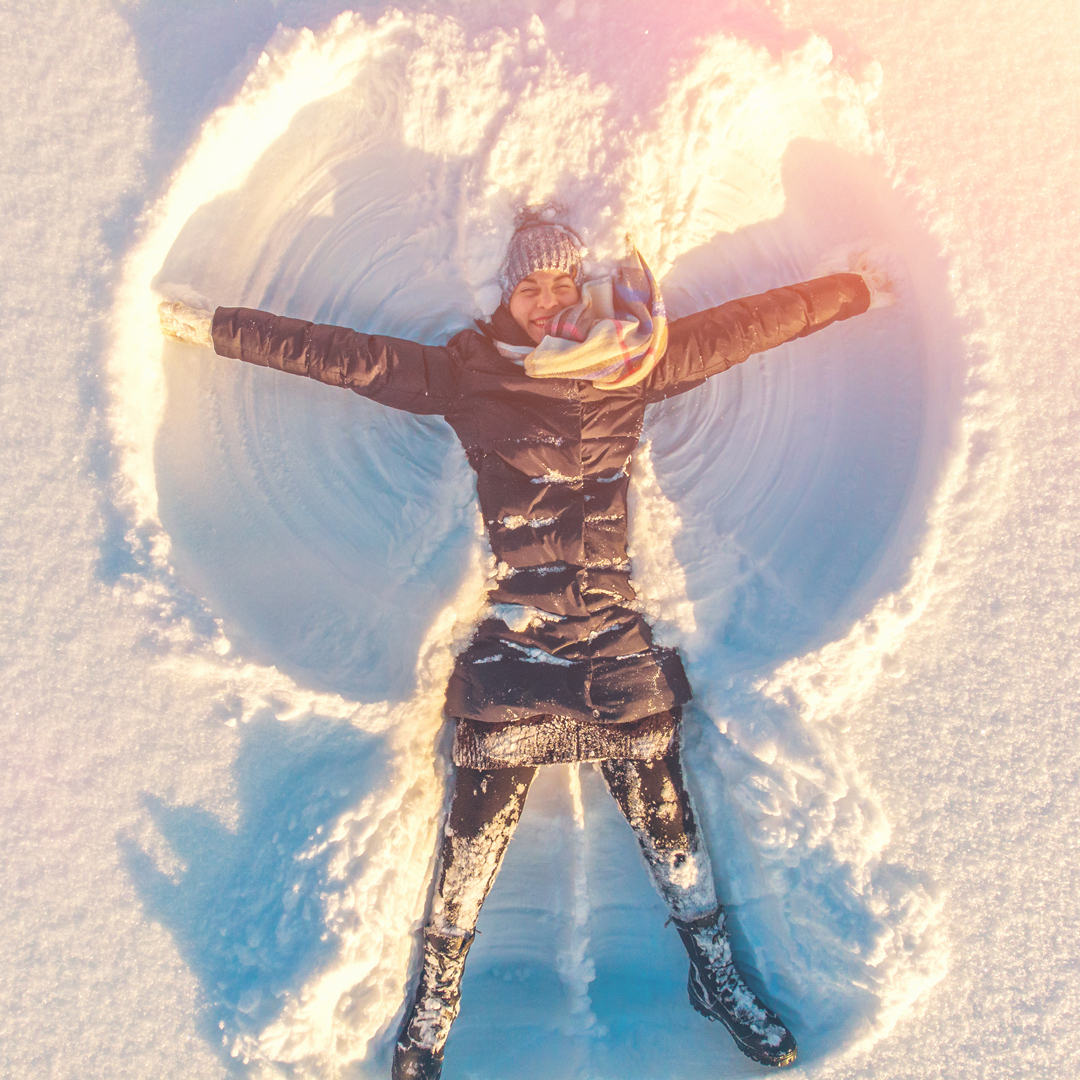 Happy woman making snow angel -- Heliocare sunblock protecting her skin from winter sun